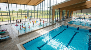 A professional, high-angle editorial photograph of a modern, sunlit indoor swimming pool facility wi